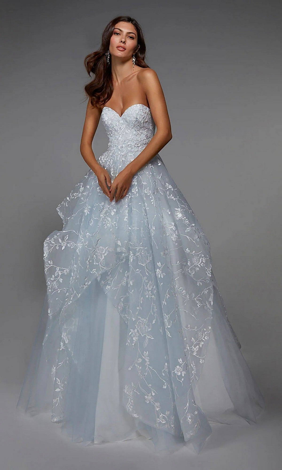 A woman in an Alyce 7041 long formal dress in Icelandic Blue/Diamond White, featuring a strapless sweetheart neckline and floral embroidery, stands against a plain gray background.